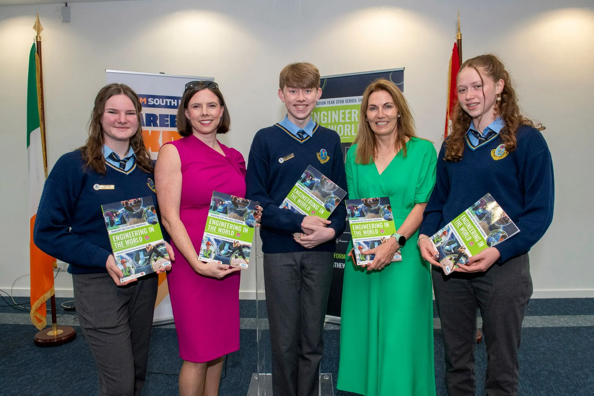 Three students in school uniform and two women, each holding a copy of the book