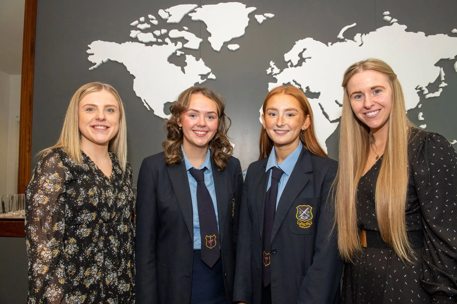 Two students in school uniform with two women in front of a world map wall